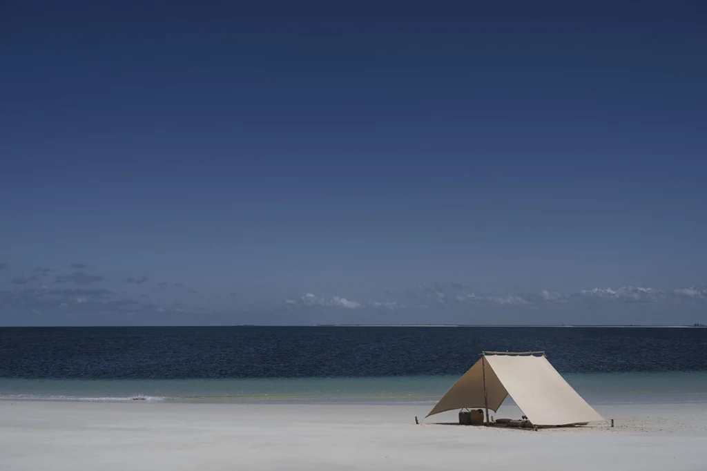 A tent on a secluded sandbank with the bright blue ocean.