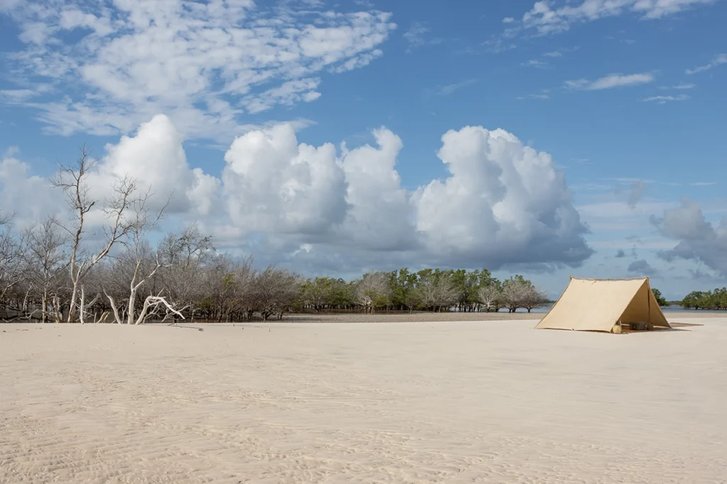 Wide-angle shot of a tent set up on a secluded lagoon bank.