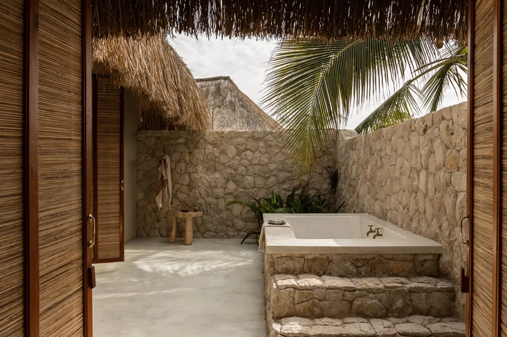 Romantic open-air bath with stone detail and palms hanging over.