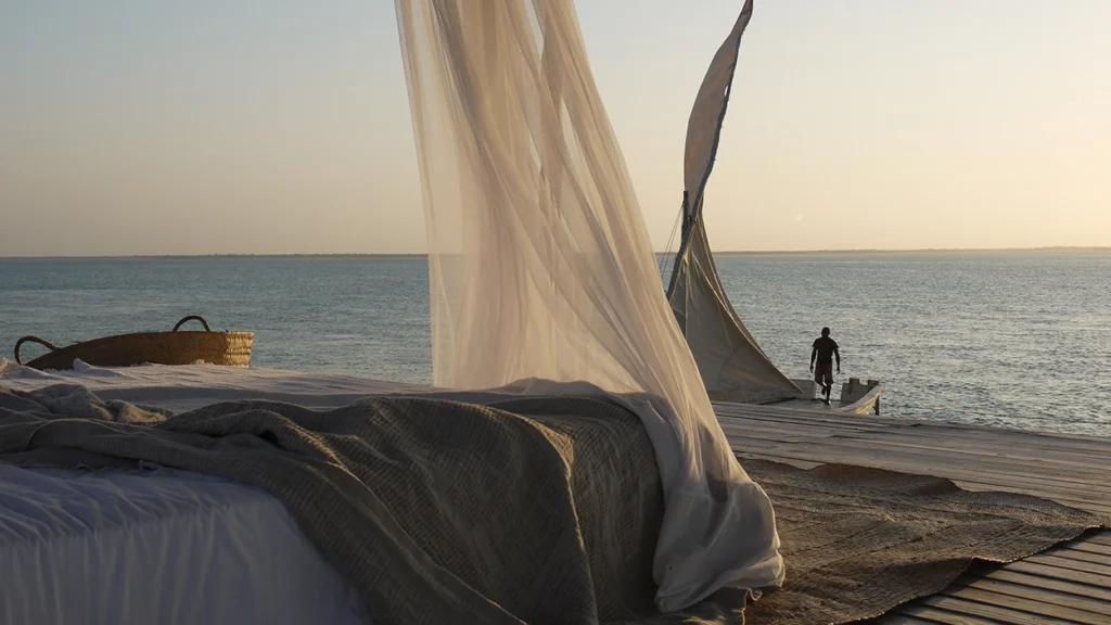 Day bead with draped fabric on an ocean deck with a dhow in the background.