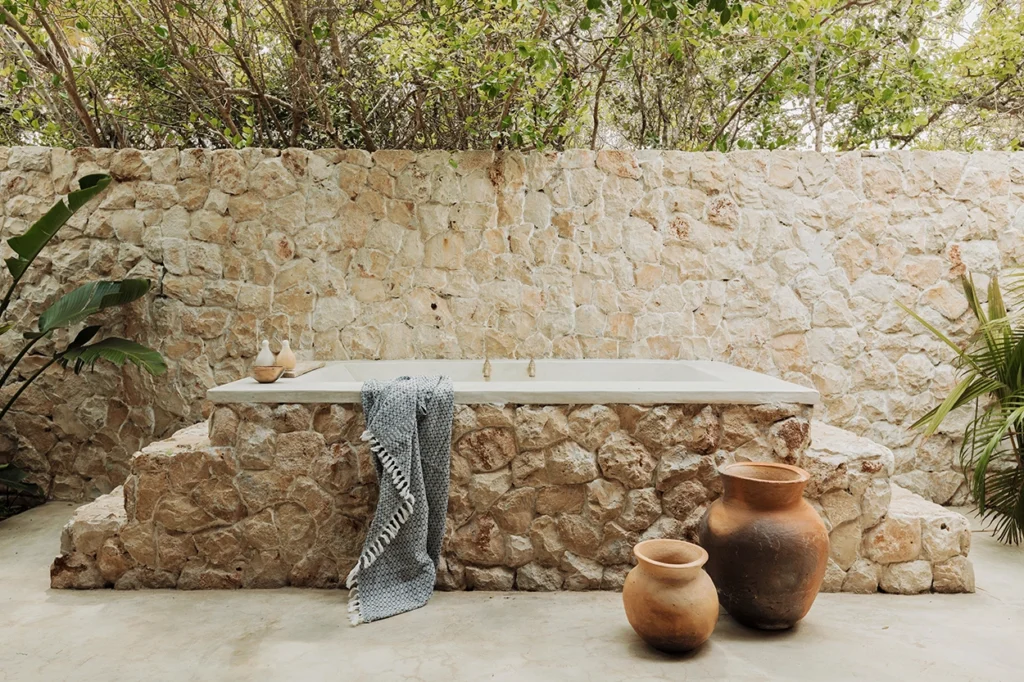 Open-air bathtub with pots and a draped towel and greenery.